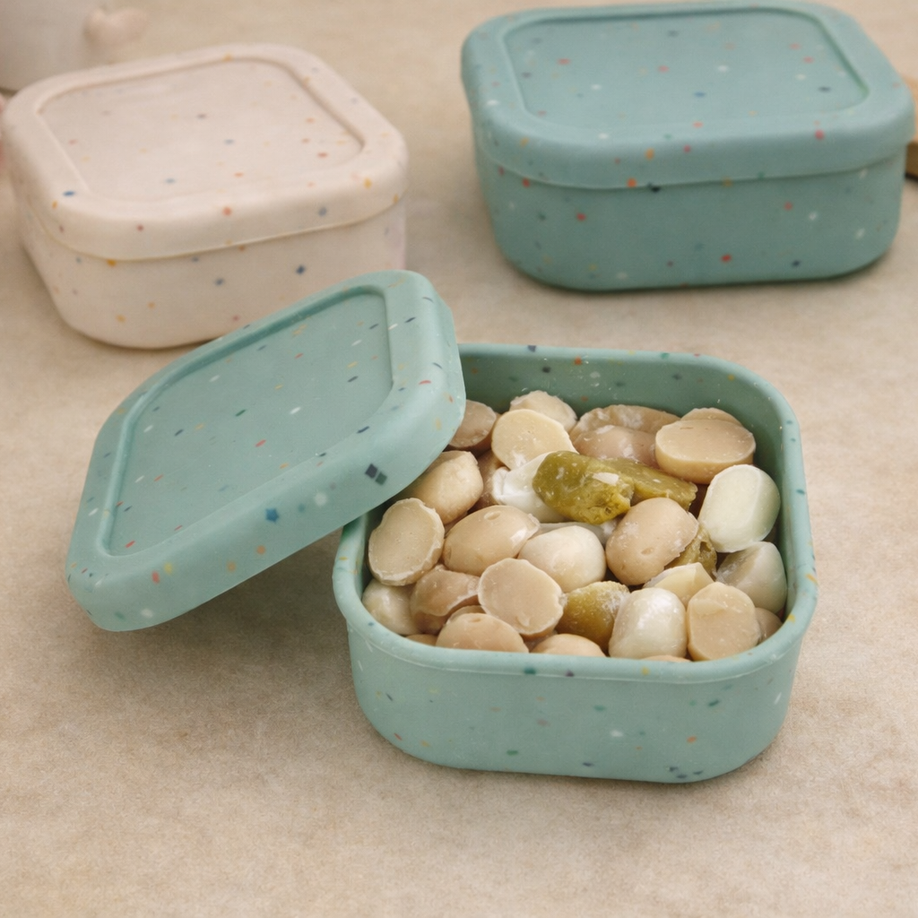 Green silicone snack container with rocks and a lid on a beige surface
