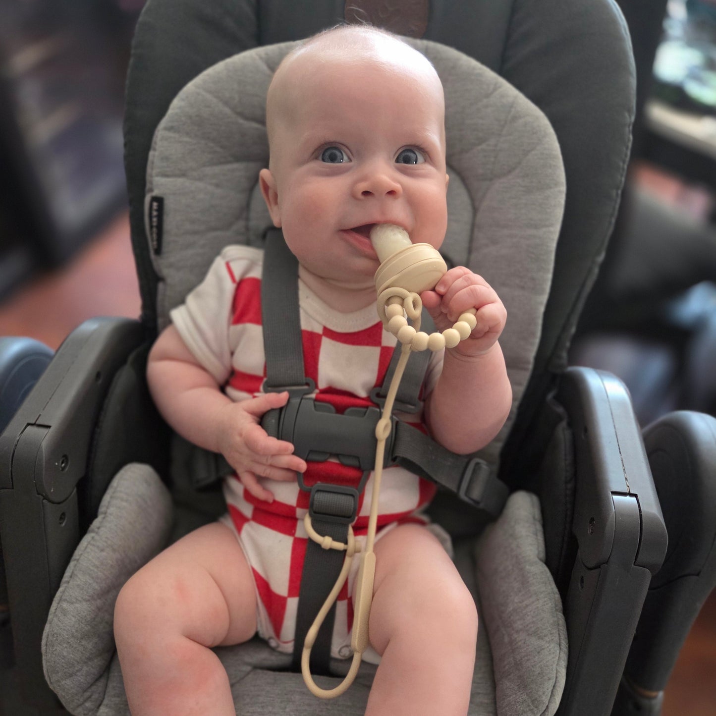 Baby in a highchair with a boobcube teething ring, looking up.
